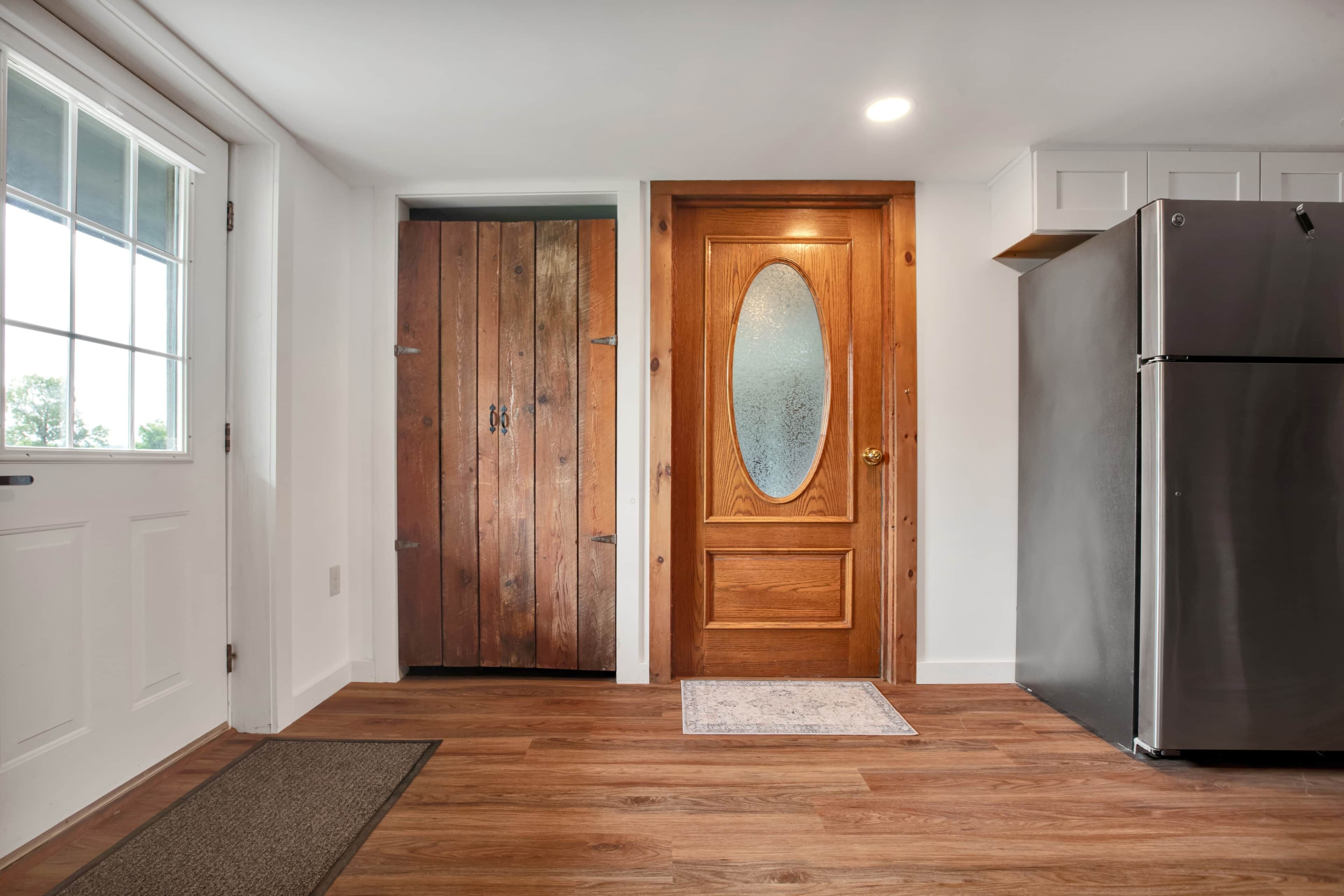 A kitchen with wooden flooring, a refrigerator, and a double door with a frosted glass window.