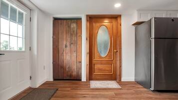 A kitchen with wooden flooring, a refrigerator, and a double door with a frosted glass window.