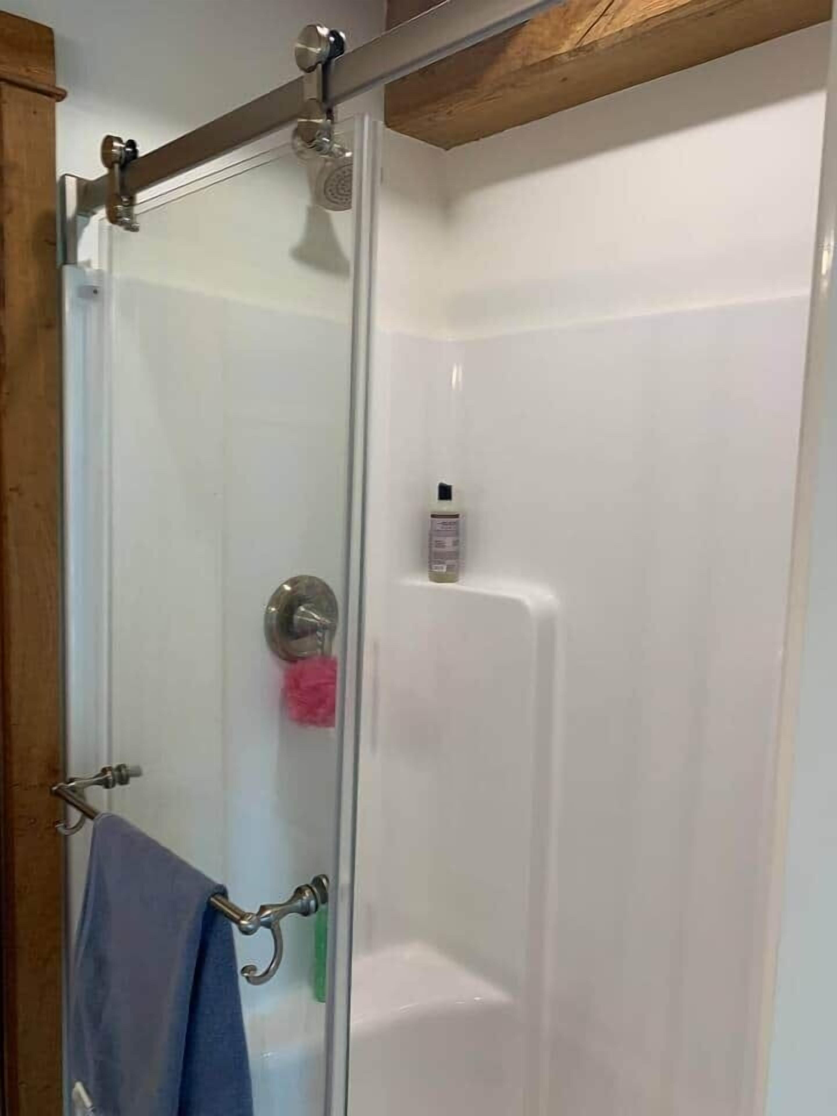 Eine Duschkabine mit Handbrause, eine kleine Shampooflasche und ein blaues Handtuch, das an einem Metallhaken hängt.