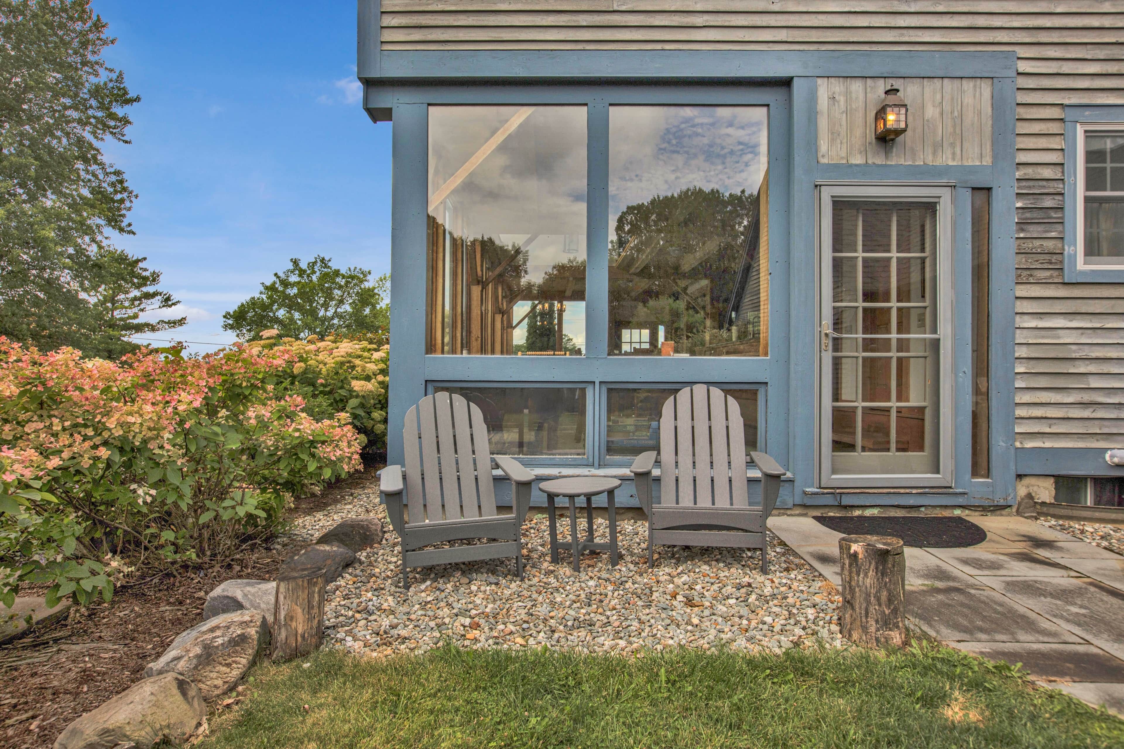 A blue building with large windows, a door, and two Adirondack chairs with a table in front.
