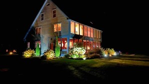 Una casa de dos pisos con un techo a dos aguas destacado, ventanas amplias y un porche delantero bien iluminado.