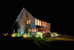 Ein zweistöckiges Haus mit markantem Giebeldach, großen Fenstern und einer gut beleuchteten Veranda.