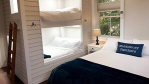 Une chambre avec des lits superposés, une table de chevet avec une lampe, une fenêtre avec des stores et un oreiller orné du texte « Middlebury Panthers ».