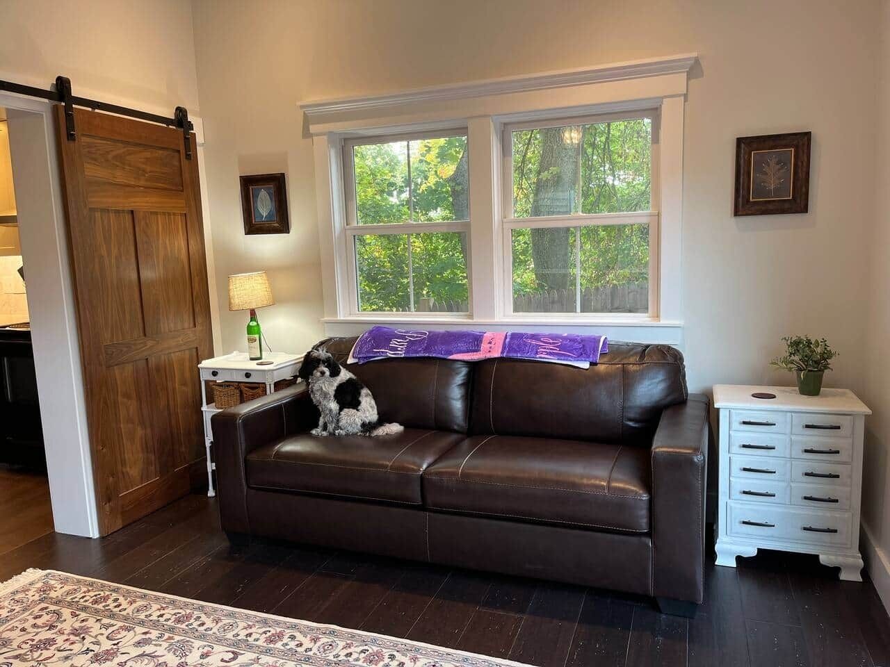 Ein braunes Ledersofa, ein weißer Beistelltisch, eine Holztür und ein Fenster mit Blick auf Bäume.