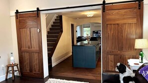 Un intérieur de maison avec une porte coulissante en bois, un escalier, un îlot de cuisine et un chien sur un canapé.