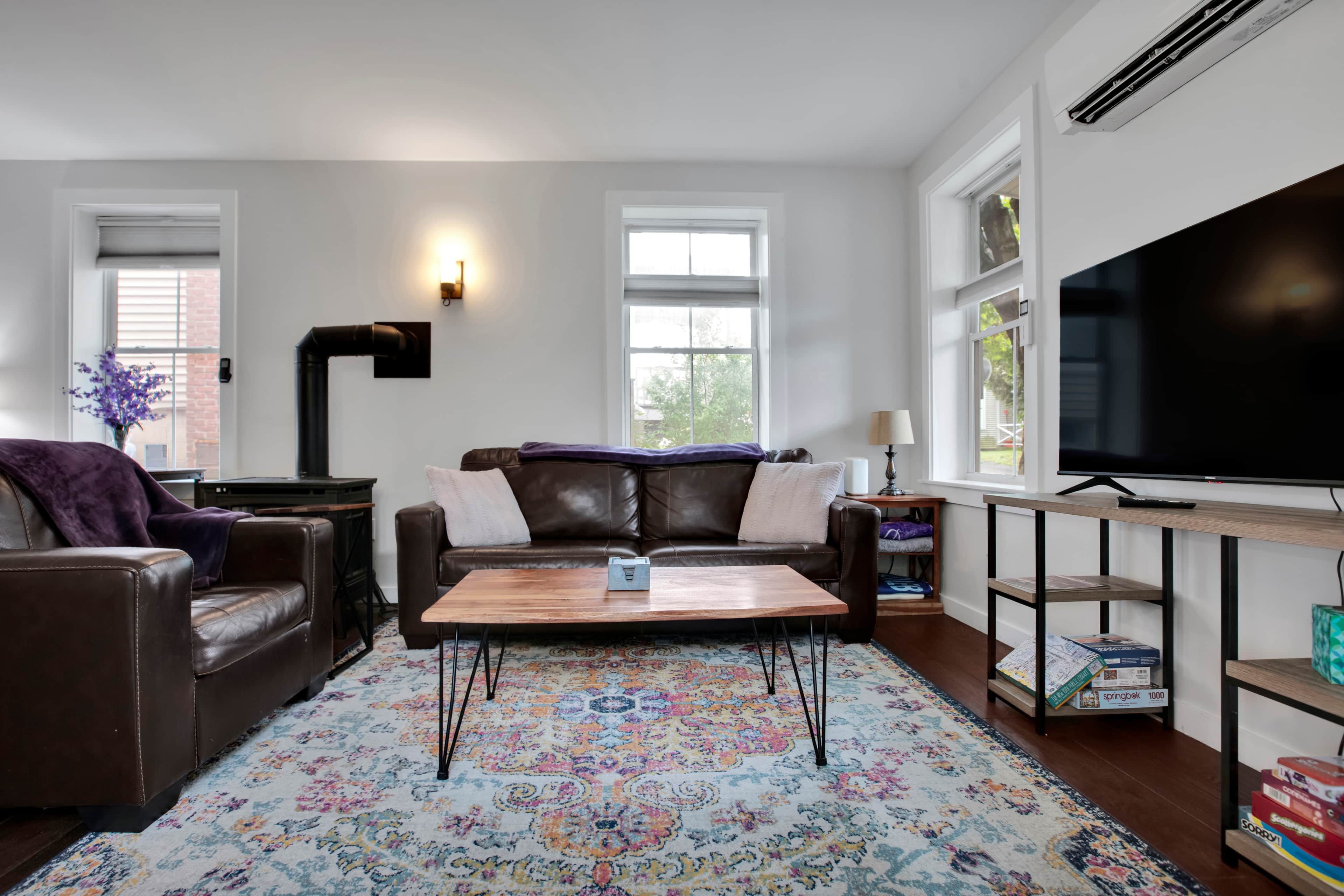 Un salon avec un canapé en cuir marron, une table basse en bois et un tapis aux motifs colorés.