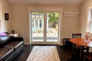 A living room with a dark leather sofa, a patterned rug, a dining table with a vase of flowers, and a sliding glass door leading to an outdoor area.