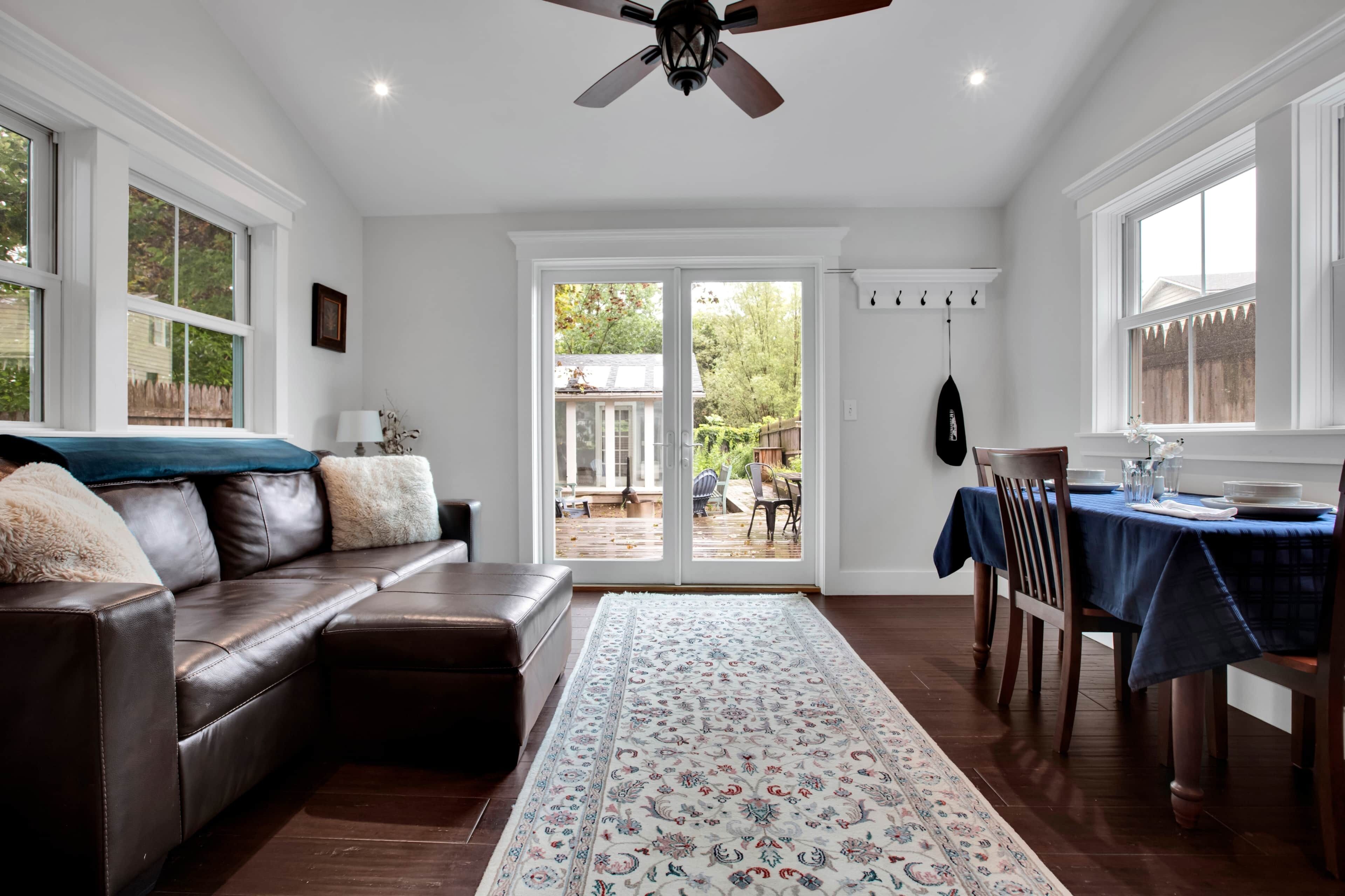 A spacious living room with a leather sofa, a dining area with a table set for two, and a view through a glass door to an outdoor patio.