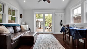 A spacious living room with a leather sofa, a dining area with a table set for two, and a view through a glass door to an outdoor patio.