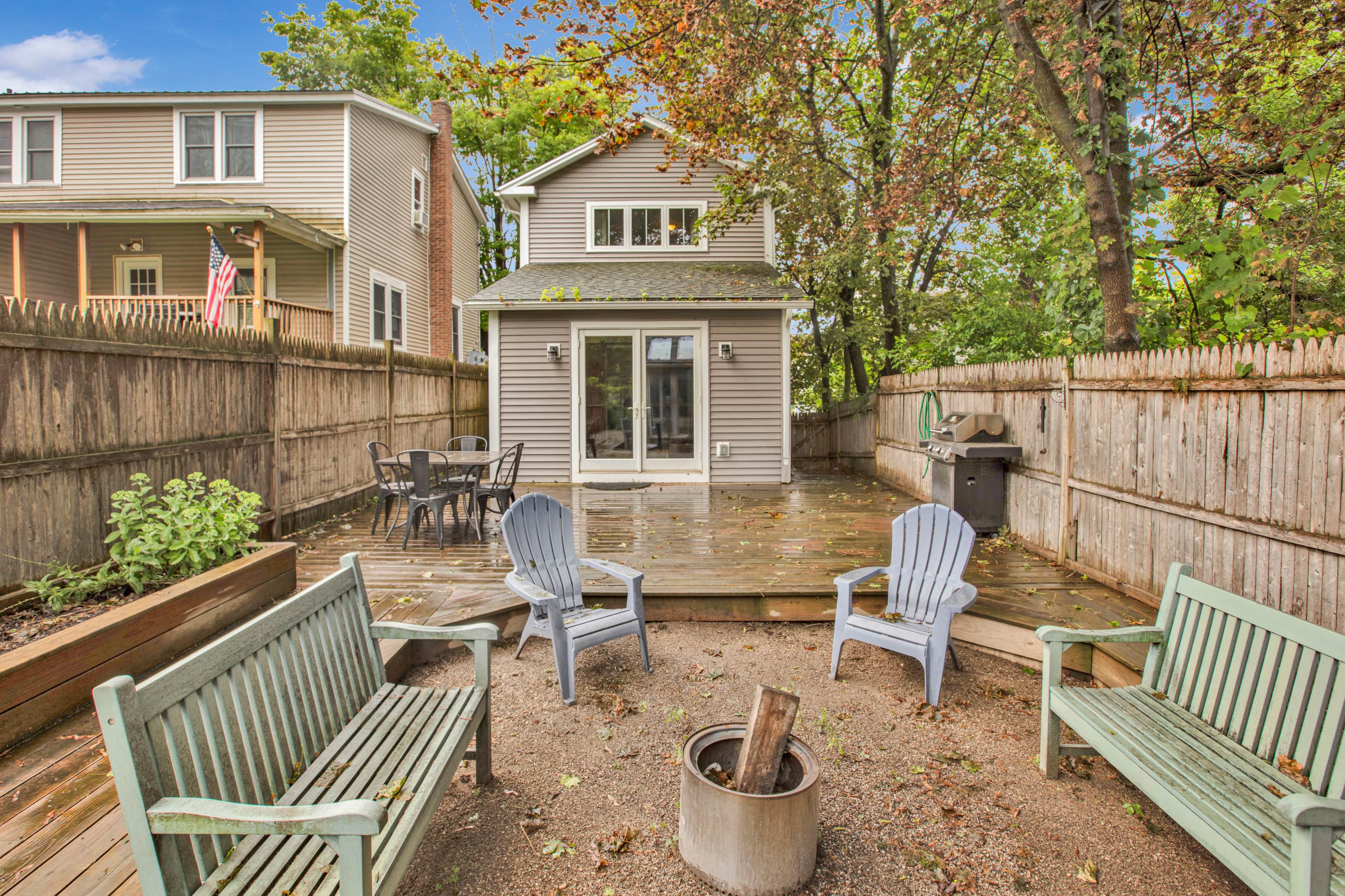A backyard with a wooden deck, two Adirondack chairs, a fire pit, and a small shed.