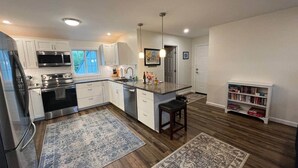 A modern kitchen with white cabinets, stainless steel appliances, a bar area, and a wooden floor. - Gracious two bedroom just minutes to Middlebury! (New Haven)
