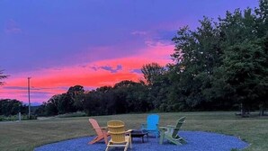 A grassy outdoor area with colorful Adirondack chairs arranged in a circle. - Gracious two bedroom just minutes to Middlebury! (New Haven)