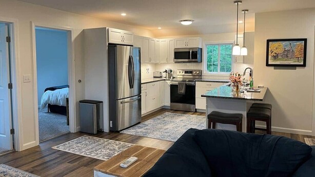 A modern kitchen with stainless steel appliances, a dining area with a table and chairs, and a living room with a sofa. - Gracious two bedroom just minutes to Middlebury! (New Haven)