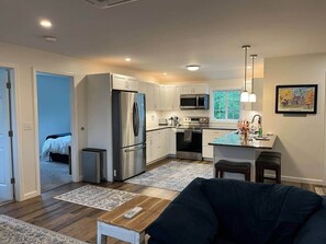 A modern kitchen with stainless steel appliances, a dining area with a table and chairs, and a living room with a sofa. - Gracious two bedroom just minutes to Middlebury! (New Haven)