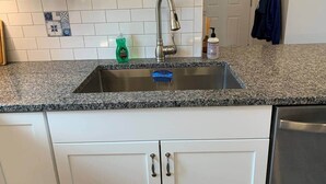 A kitchen with a granite countertop, white cabinets, a stainless steel sink, and a dishwasher. - Gracious two bedroom just minutes to Middlebury! (New Haven)