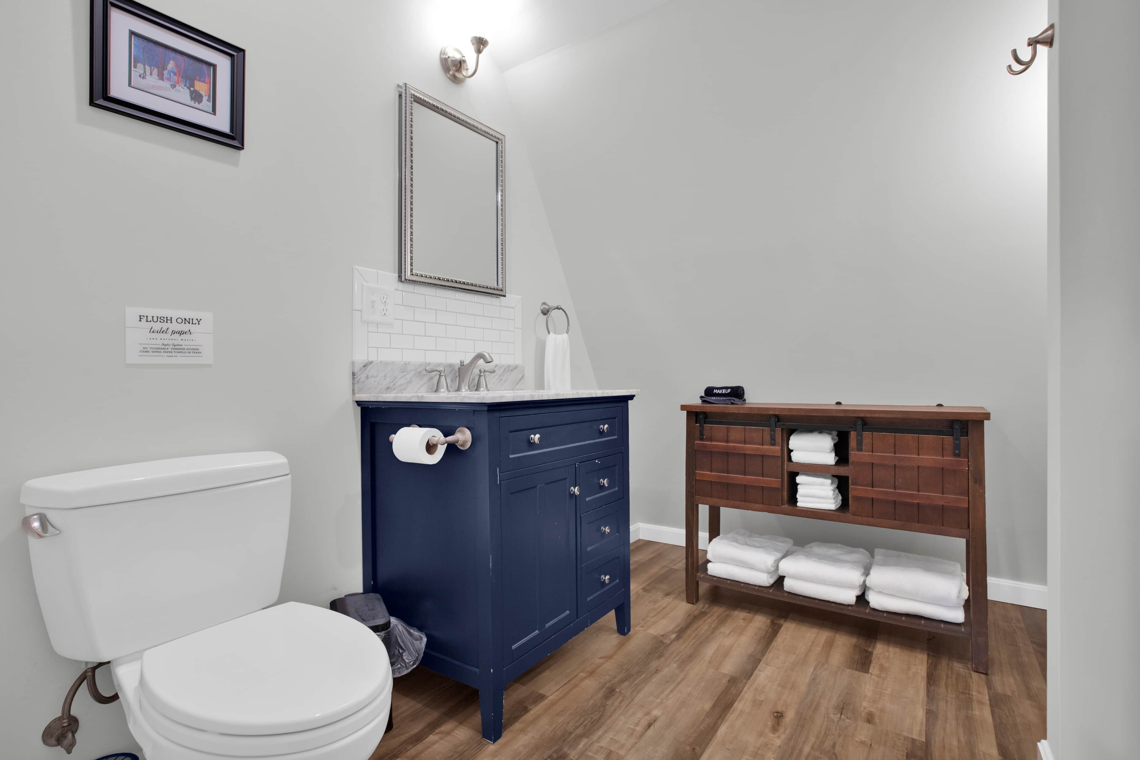Une salle de bain comprenant des toilettes, un meuble-lavabo avec un miroir et une étagère en bois où sont posées des serviettes.