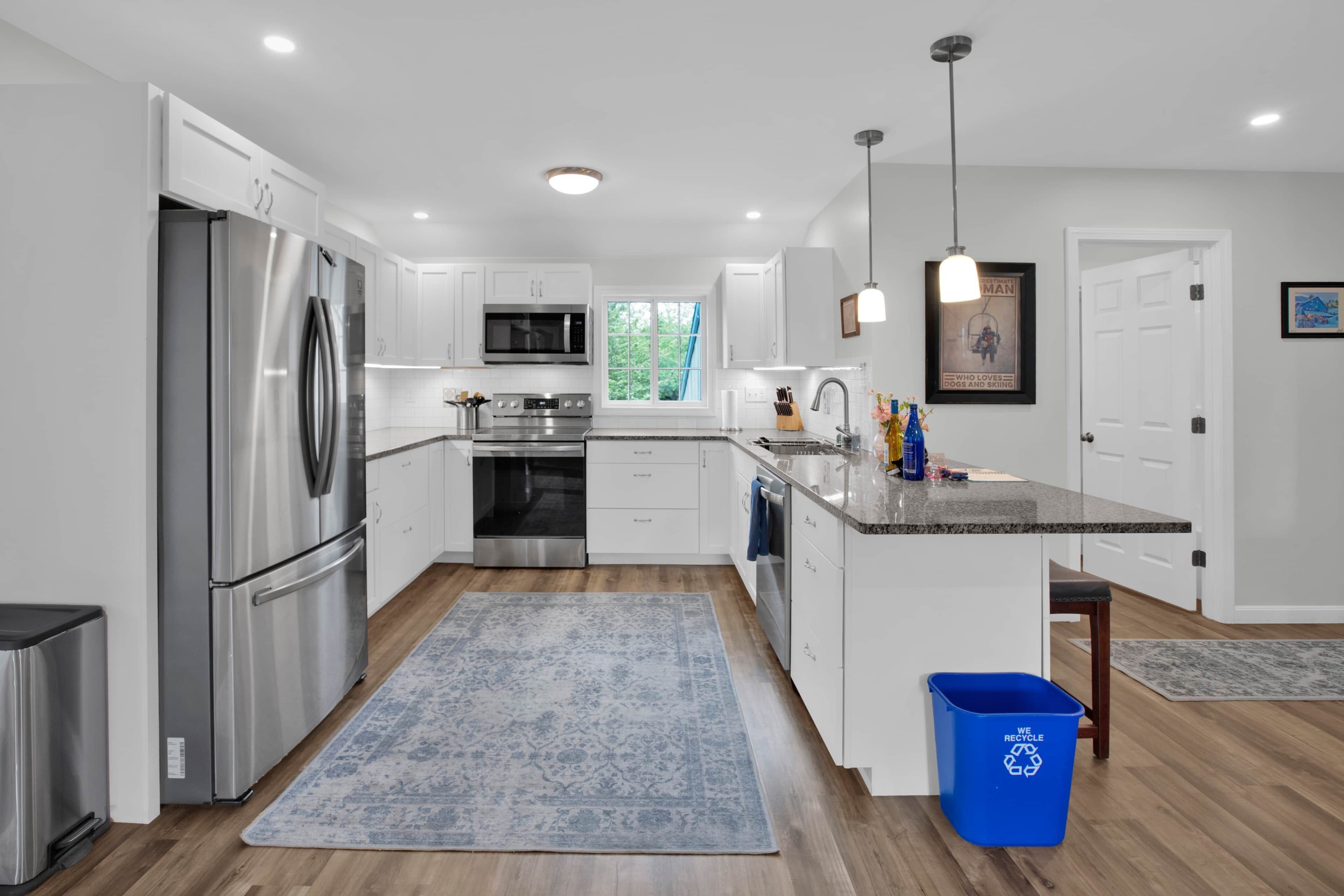 A modern kitchen with stainless steel appliances, white cabinetry, and a blue recycling bin.