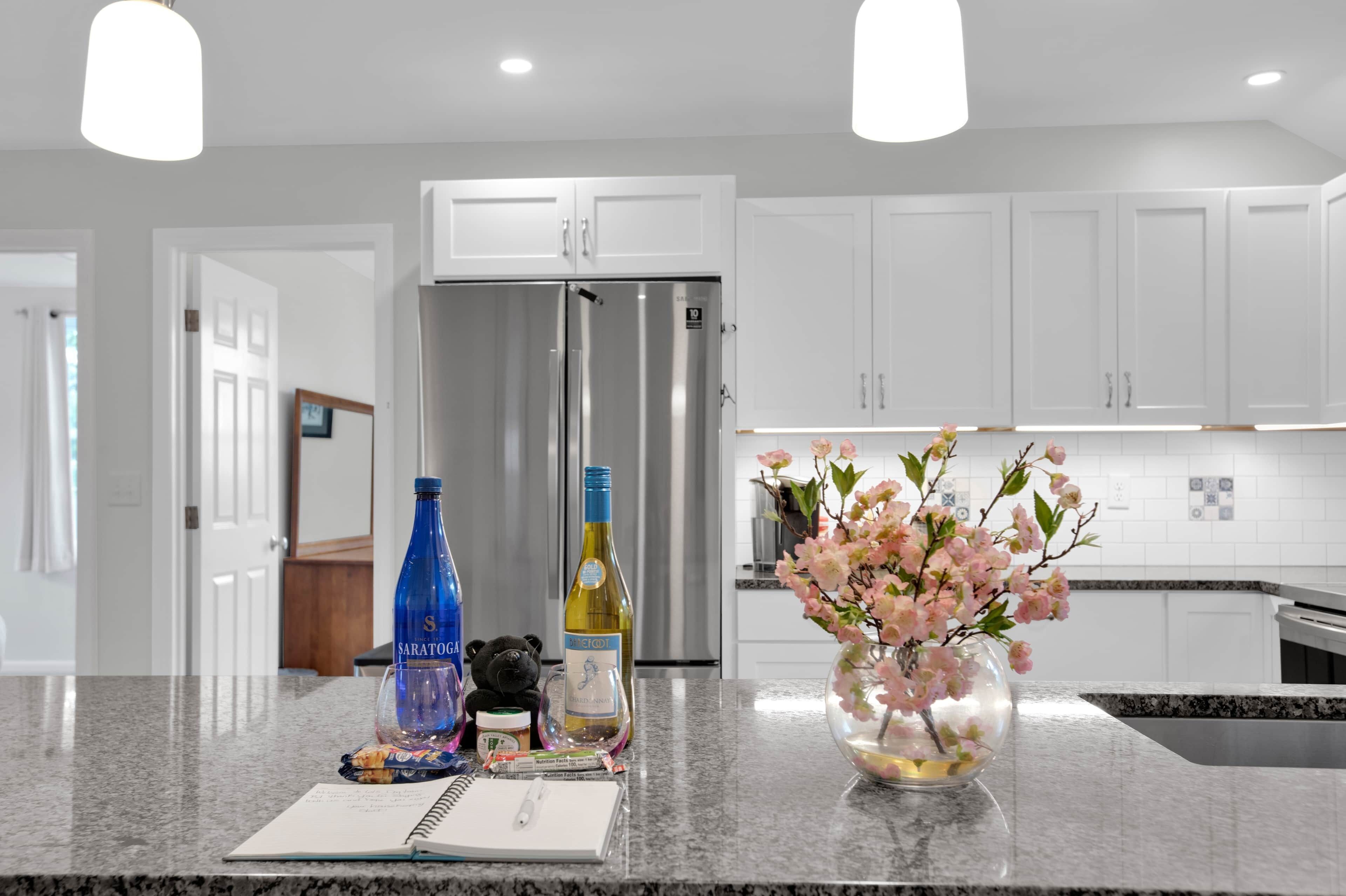 A kitchen with white cabinets, a stainless steel refrigerator, a vase with pink flowers, and a notebook on the counter.