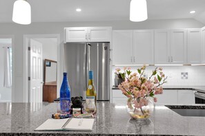 A kitchen with white cabinets, a stainless steel refrigerator, a vase with pink flowers, and a notebook on the counter.