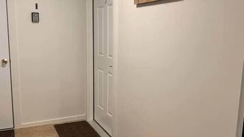 Un pasillo con un banco de madera, un tapete estampado, una puerta con número y un cartel en la pared.
