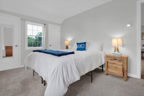 A bedroom with a bed, a nightstand, a lamp, a window, and a door.