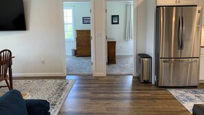 A living room with a large flat-screen TV, a wooden chair, a patterned rug, and a stainless steel refrigerator. - Gracious two bedroom just minutes to Middlebury! (New Haven)