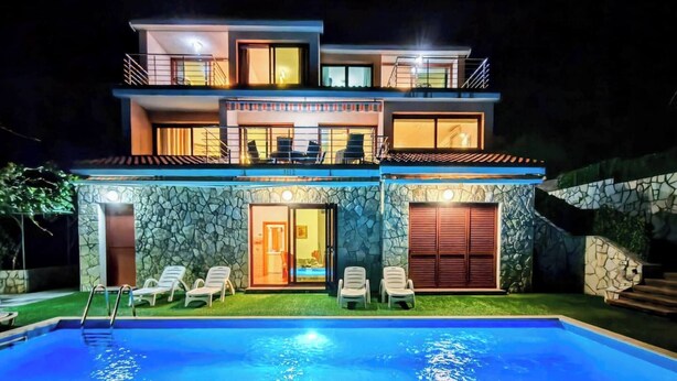 Une maison moderne à deux étages, dotée d’une piscine, d’un espace salon extérieur et d’une façade en pierre.