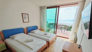 Une chambre d’hôtel avec deux lits, un balcon avec une table et des chaises, et un téléviseur fixé au mur.