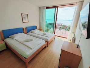 A hotel room with two beds, a balcony with a table and chairs, and a TV on the wall. - Villa Vrata Jadrana 1 (Rijeka)