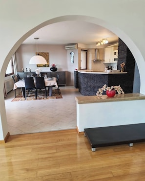 A modern kitchen with a stone island, a dining area with a table and chairs, and a large arched doorway leading to another room. - Villa Vrata Jadrana 1 (Rijeka)