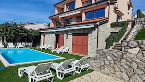 Un bâtiment à deux étages doté d’une piscine, de chaises longues et d’un mur en pierre.