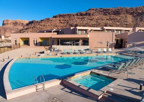 A pool area with lounge chairs and umbrellas, a pool with a diving board, and a building with multiple balconies.