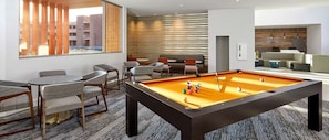A pool table with chairs and tables, a sofa, and a view of buildings outside.