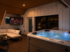A hot tub in a room with a wooden ceiling, a white couch, and a large window. - Modern Columbus Retreat Hot Tub, Theater, Games, Sleeps 16+ (Columbus)
