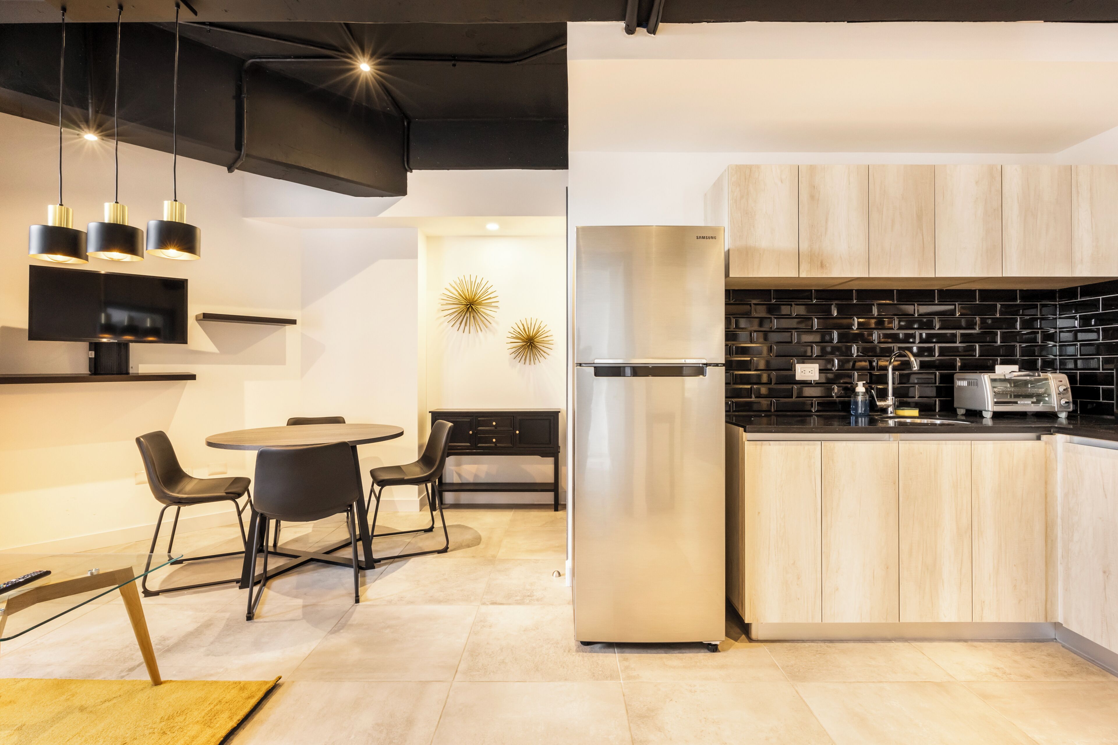 A modern kitchen with a stainless steel refrigerator, black backsplash, and wooden cabinets.