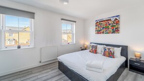 Een slaapkamer met een groot bed, twee nachtkastjes, een radiator en twee ramen.