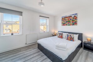 A bedroom with a large bed, two bedside tables, a radiator, and two windows. - 4 Bed Town House, 10 min walk to Bicester Village - Pass the Keys (Bicester)