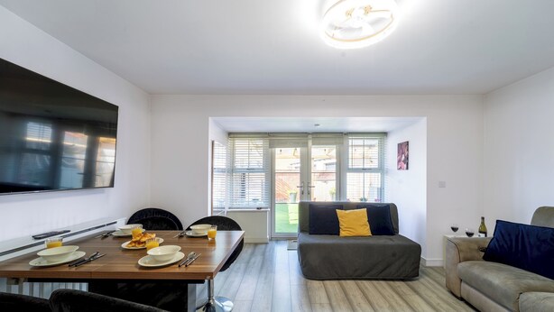 Een moderne woonruimte met een eethoek, een bank en een aan de muur bevestigde televisie.