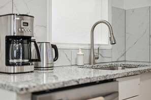 A kitchen with a coffee maker, a kettle, a soap dispenser, and a modern faucet.