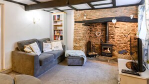 Een gezellige woonkamer met een stenen open haard, een bank, een boekenkast en een televisie.