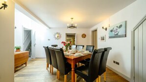 Een eetgedeelte met een houten tafel, zwarte stoelen, een kroonluchter en een schilderij aan de muur.