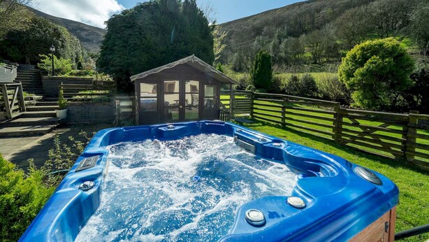 Een hottub in een tuin met een houten blokhut en een berg op de achtergrond.