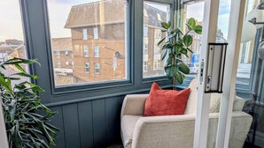 Een hoekappartement met raam, een beige bank, een rode kussens en een potplant.