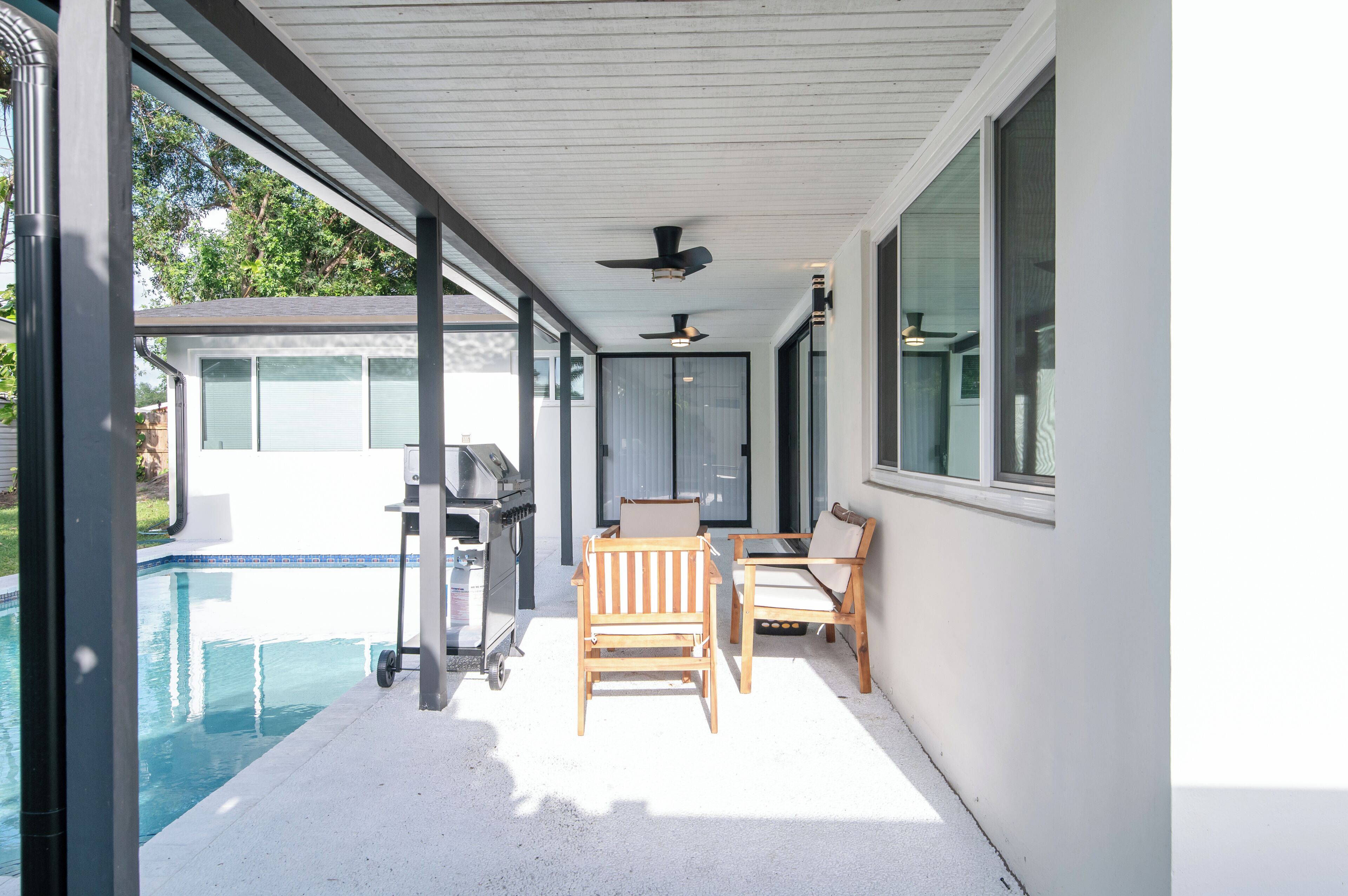 An outdoor patio with a pool, a grill, and two wooden chairs.