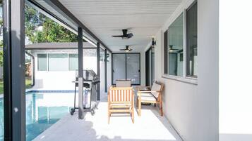 An outdoor patio with a pool, a grill, and two wooden chairs.