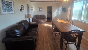 A living room with a leather sofa, a wooden dining table, and chairs. There is a ceiling fan, a lamp, and framed pictures on the walls. - Romantic Seclusion Lake Norfork Cottage 10 w/Jacuzzi at Teal Point Resort w/private lake access (Mountain Home)