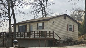 A single-story house with a front deck, a barbecue grill, and a stone wall in the background. - Romantic Seclusion Lake Norfork Cottage 10 w/Jacuzzi at Teal Point Resort w/private lake access (Mountain Home)