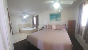 A bedroom with a bed, a ceiling fan, a bathtub, and a painting on the wall. - Romantic Seclusion Lake Norfork Cottage 10 w/Jacuzzi at Teal Point Resort w/private lake access (Mountain Home)
