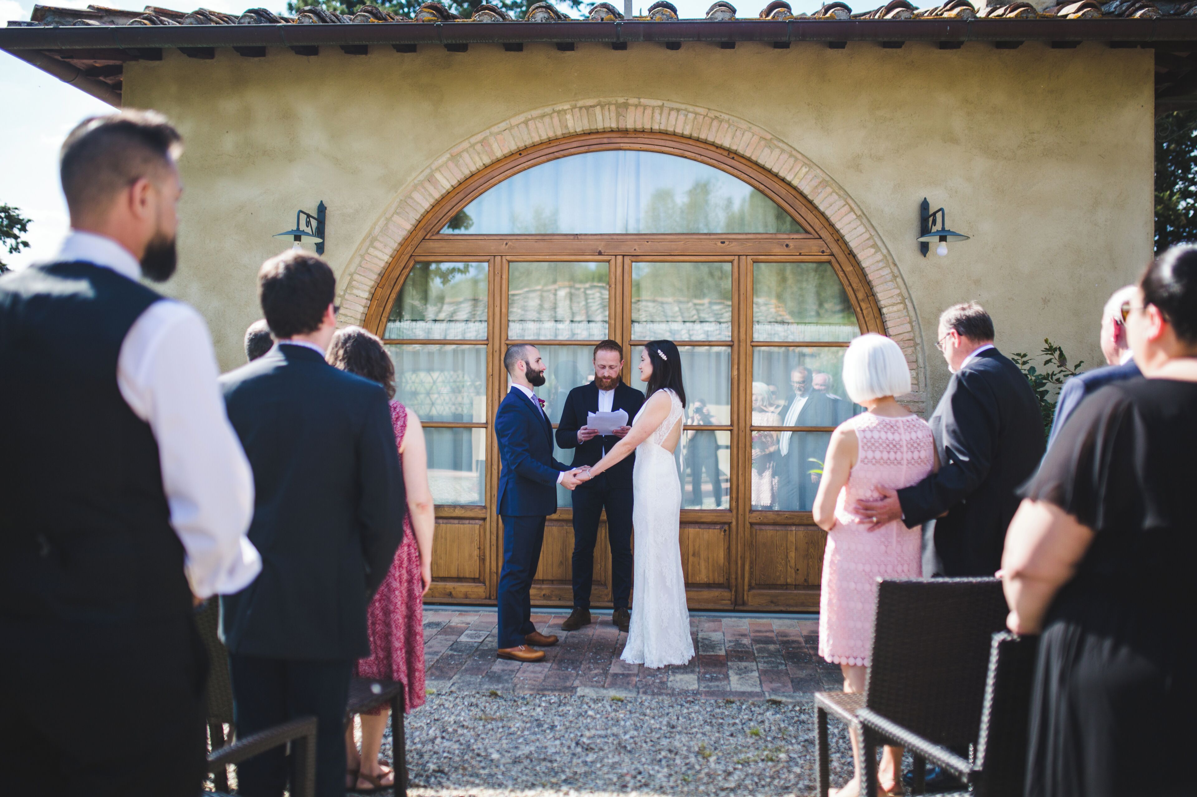 A wedding ceremony with a couple exchanging vows in front of a large arched window.