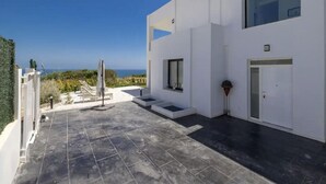 Un edificio moderno con techo plano, un pequeño espacio al aire libre con sillas y una mesa, y vistas al mar.